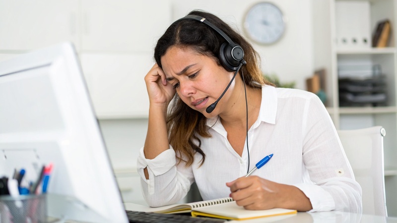 Persona con audífonos y expresión cansada frente a un computador, esperando en una llamada